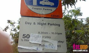 A parking sign with phrases pasted on it, making it hard to read.